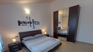 A modern bedroom with a large bed, a wardrobe, a nightstand, and a wall-mounted artwork.