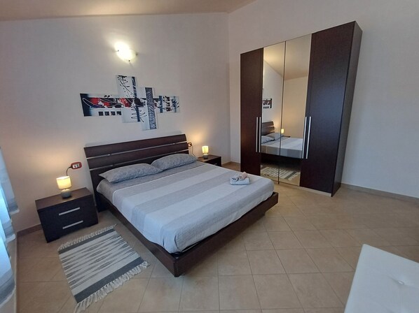 A modern bedroom with a large bed, a wardrobe, a nightstand, and a wall-mounted artwork.