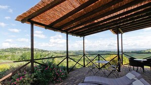An outdoor patio with a thatched roof, wicker lounge chairs, and a view of the countryside. - Villa in a panoramic position in San Gimignano (San Gimignano)