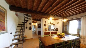 A rustic interior with a wooden dining table, green chairs, a staircase, and a kitchen area. - Villa in a panoramic position in San Gimignano (San Gimignano)
