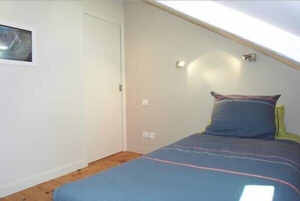 A small, single-bed room with a sloped ceiling, a window, and a wall-mounted light fixture. - Fisherman's cottage 200 m from the sea in the heart of a listed historic village (Arzon)