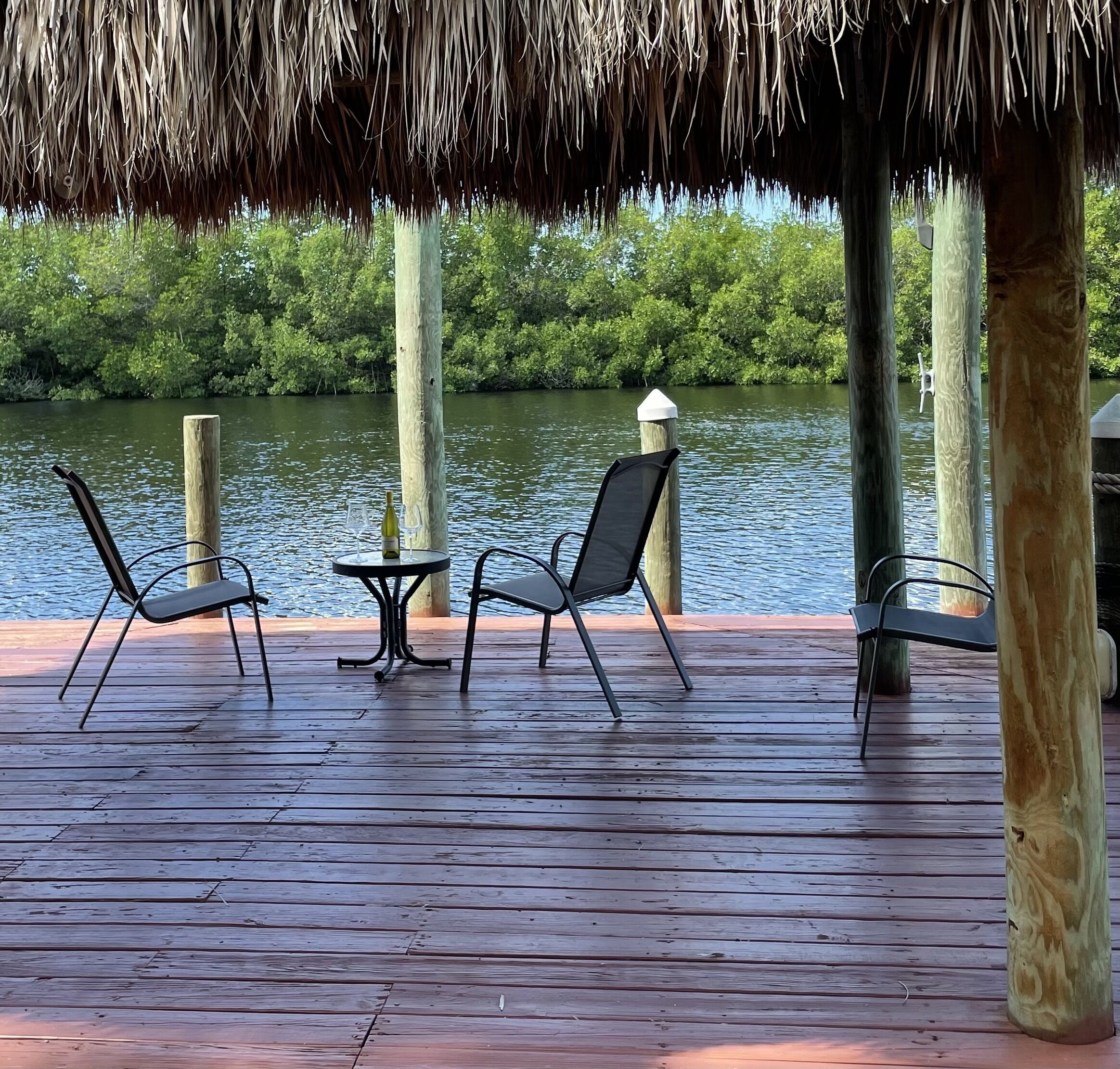 A wooden deck with two chairs and a table, overlooking a body of water with trees in the background.