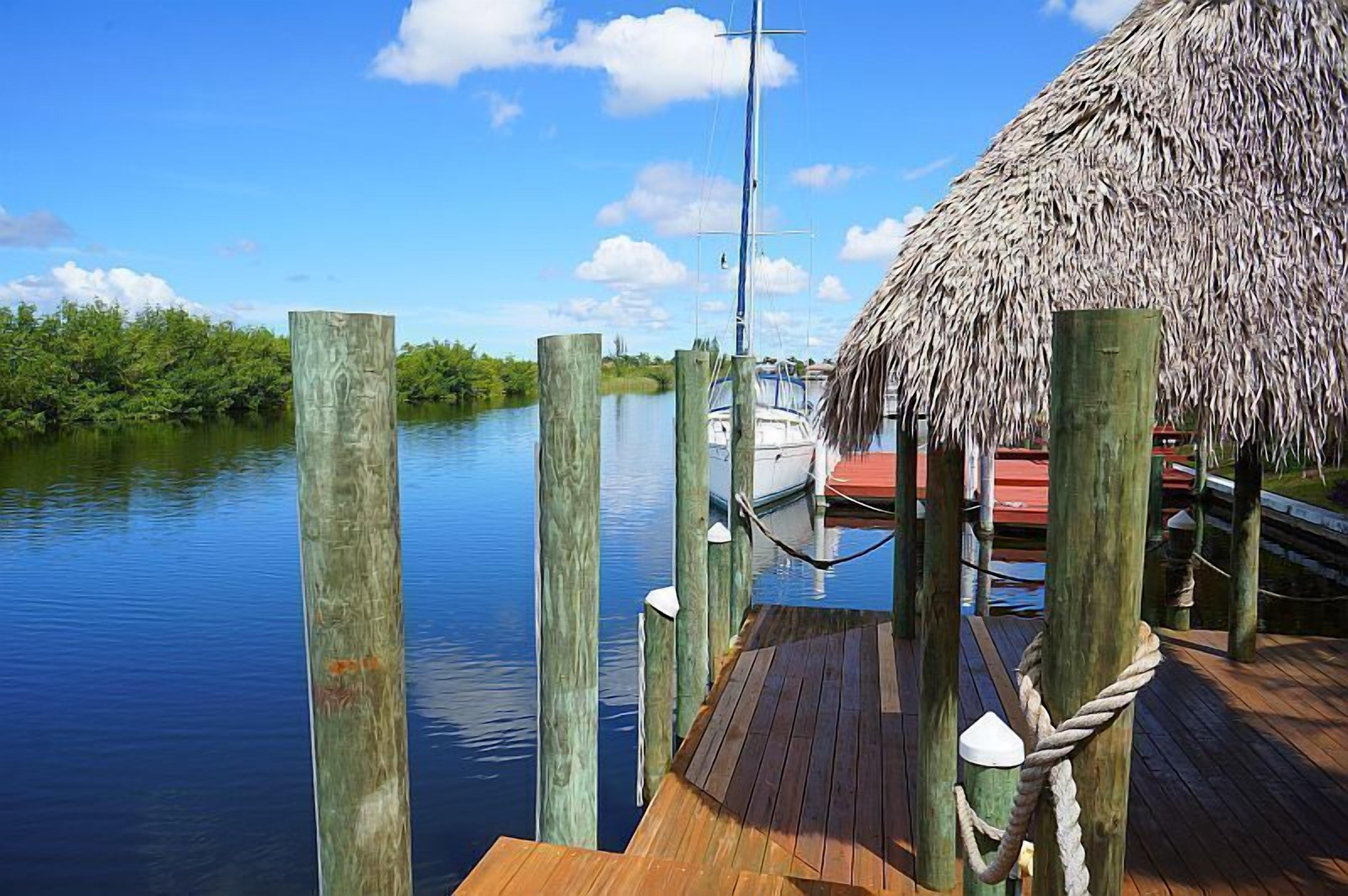 A wooden dock extending into calm water, a thatched-roof structure, and a boat docked nearby.