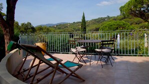Une terrasse avec une table et des chaises, une poubelle, et une vue sur un paysage verdoyant, avec des arbres et des collines.