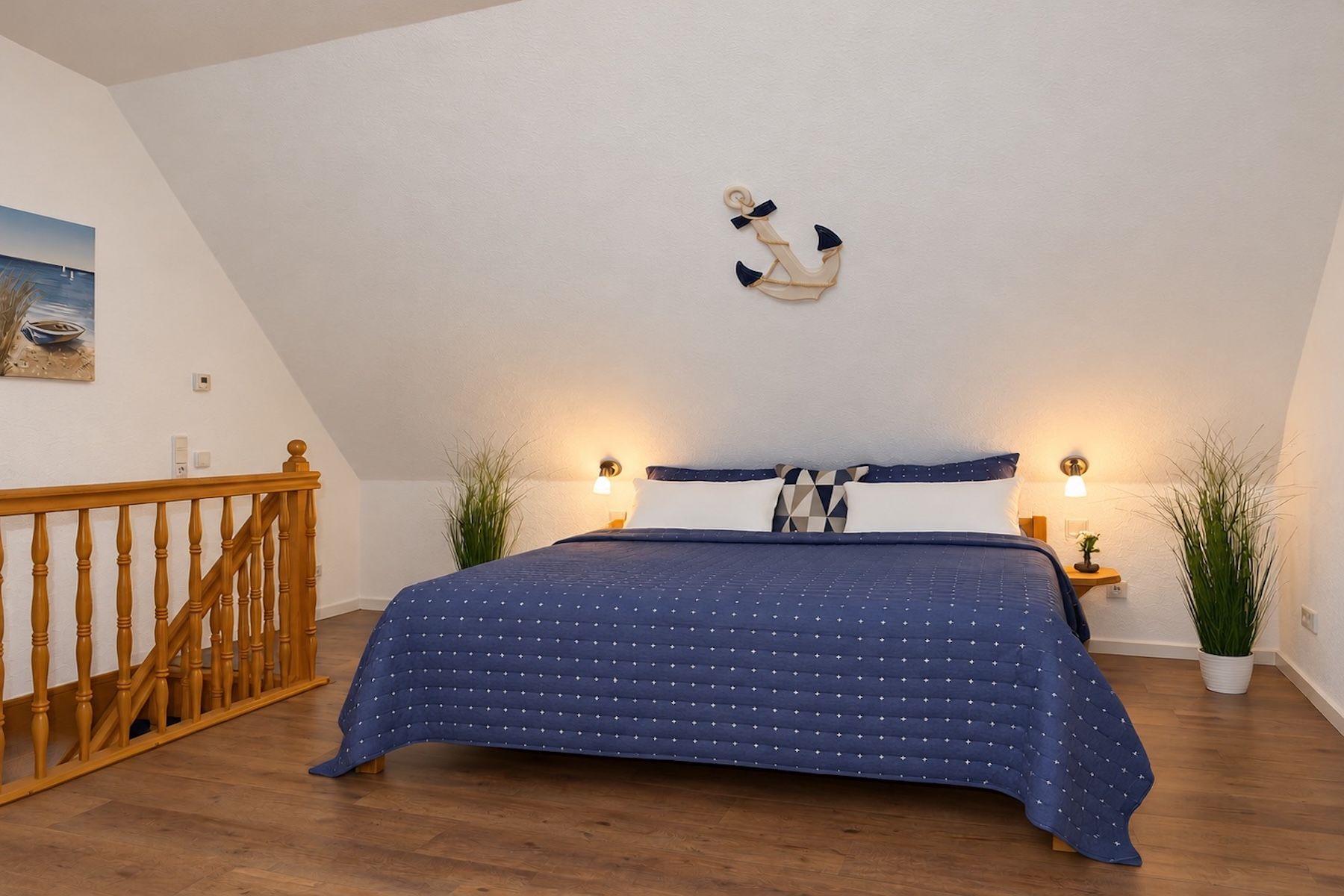 A bedroom with a wooden staircase, a bed with a blue bedspread, two bedside lamps, and a wall-mounted anchor decoration.