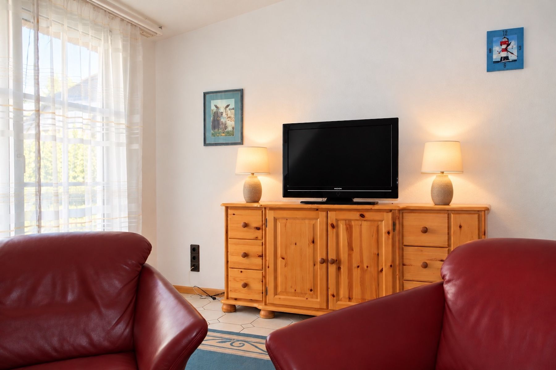 Un salon avec un téléviseur posé sur un meuble en bois, deux lampes et un tableau accroché au mur.