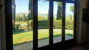 Un ventanal grande con vista a un jardín, un banco y árboles altos.