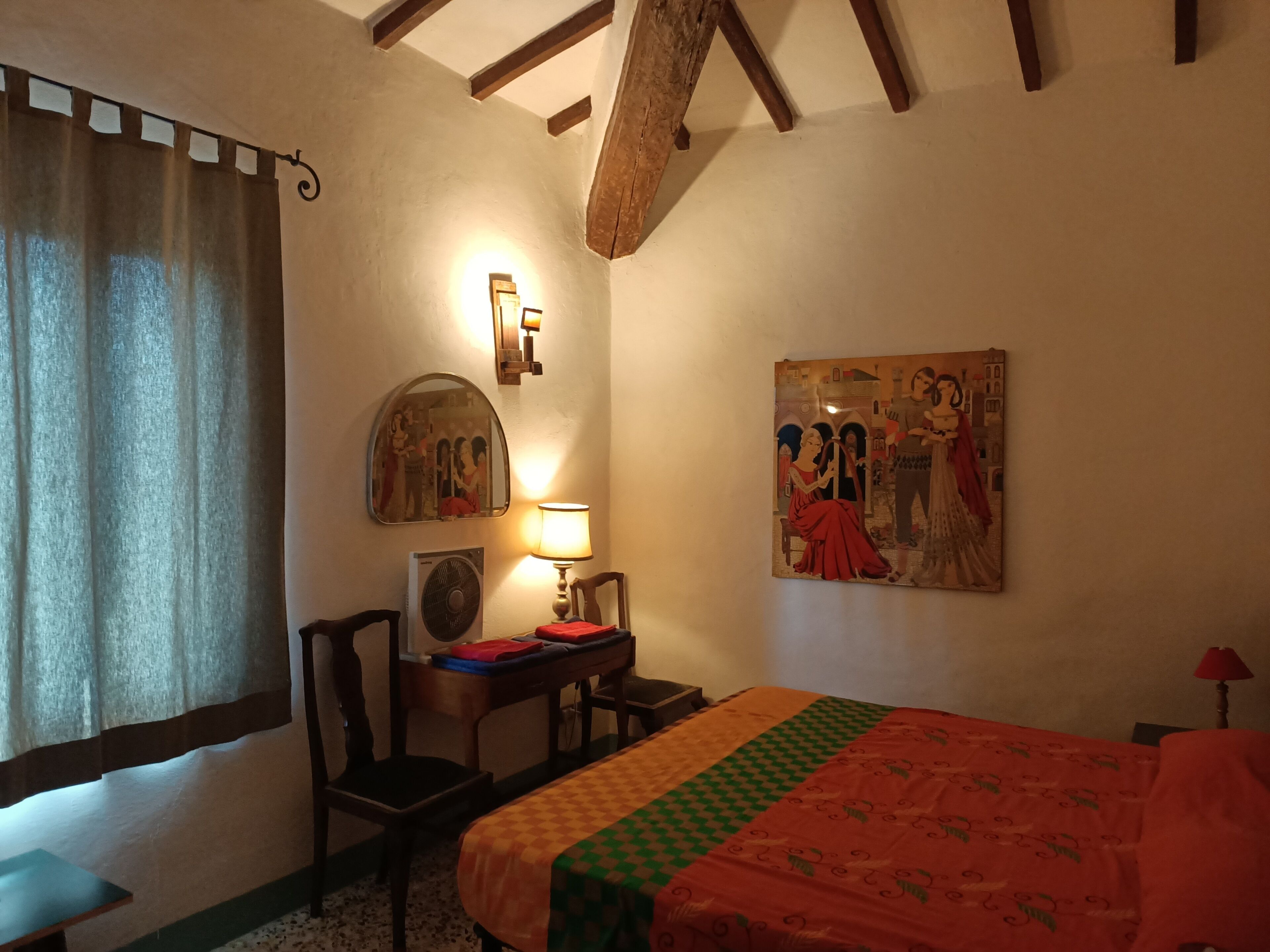 Ein Hotelzimmer mit Bett, Schreibtisch, Stuhl, Lampe, Spiegel und einem Bild an der Wand.