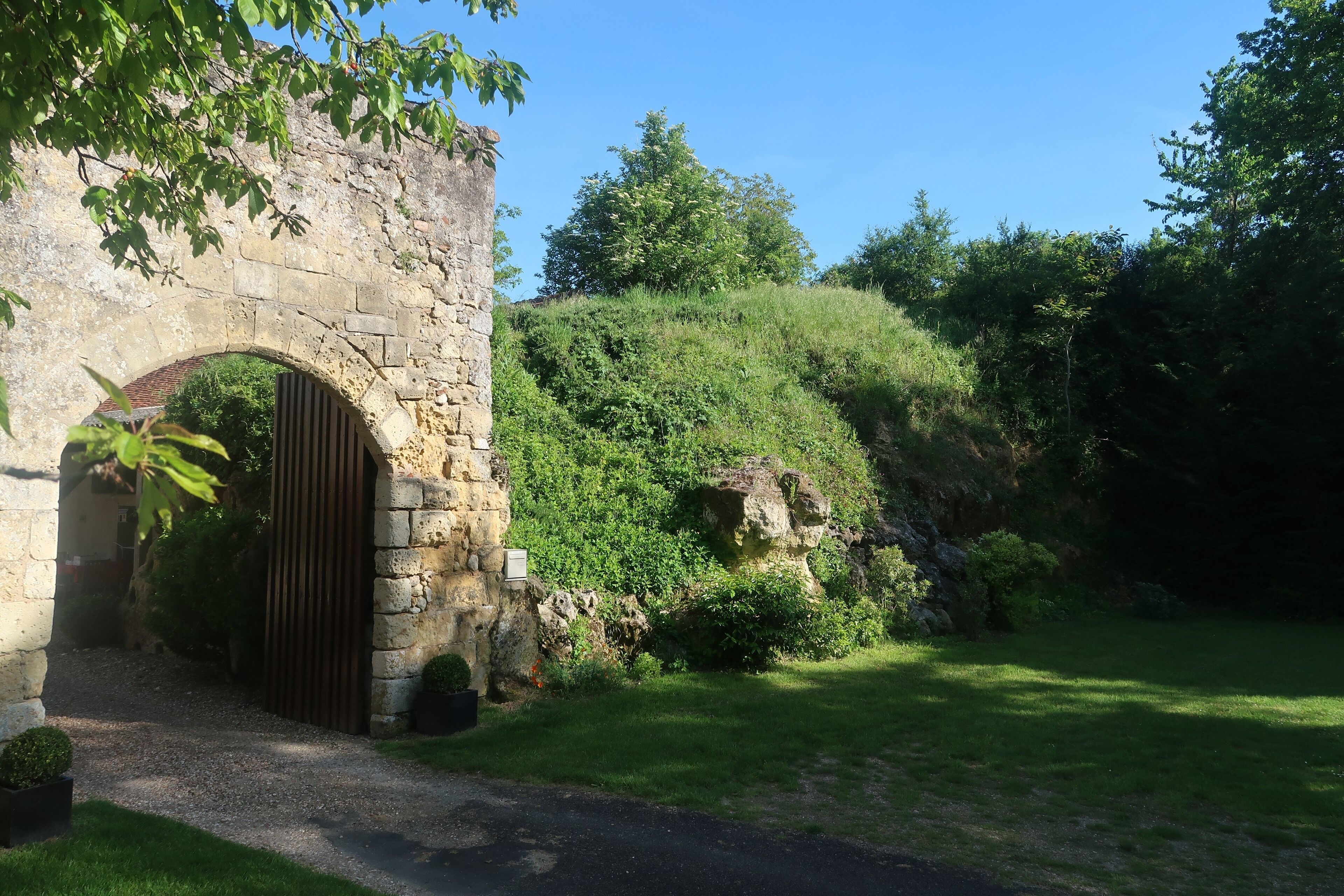 An arched stone entrance to a building surrounded by lush greenery and a hill.