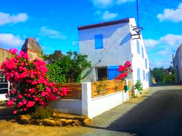 Una calle estrecha con un edificio blanco que tiene un ventanal azul y un pequeño balcón.