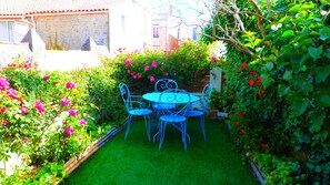 Un jardin agrémenté d’une table et de chaises, entouré d’une végétation luxuriante et de plantes en fleurs.