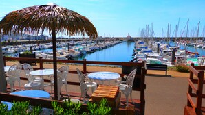A marina with numerous boats docked, a thatched umbrella, and outdoor seating with tables and chairs.
