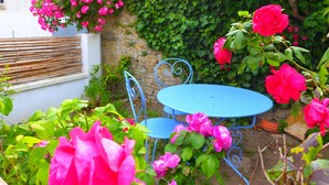 A blue metal table and chair set in a garden with blooming pink roses and a stone wall.