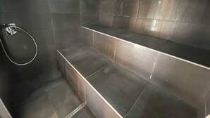 Une salle de bain moderne avec des murs recouverts de carreaux foncés, un espace douche et un banc.