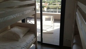 Une chambre avec un lit superposé, un balcon avec une porte vitrée et une vue sur un paysage verdoyant.