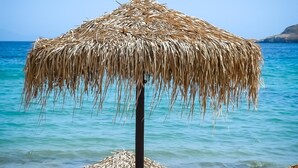 En strandscene med en stråtagsparasol, to liggestole og et bord dækket med et blåt og hvidt mønstret stof.