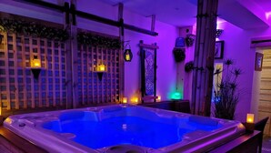 Ein Whirlpool mit Holzterrasse, umgeben von Pflanzen und dekorativer Beleuchtung.