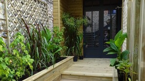 Eine Holzterrasse mit erhöhten Pflanzkästen, einer Steinmauer und einer Holztür.