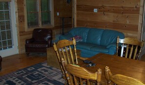 L’intérieur d’un chalet en bois comprend une table à manger, des chaises, un fauteuil en cuir, un canapé bleu et un tapis à motifs.