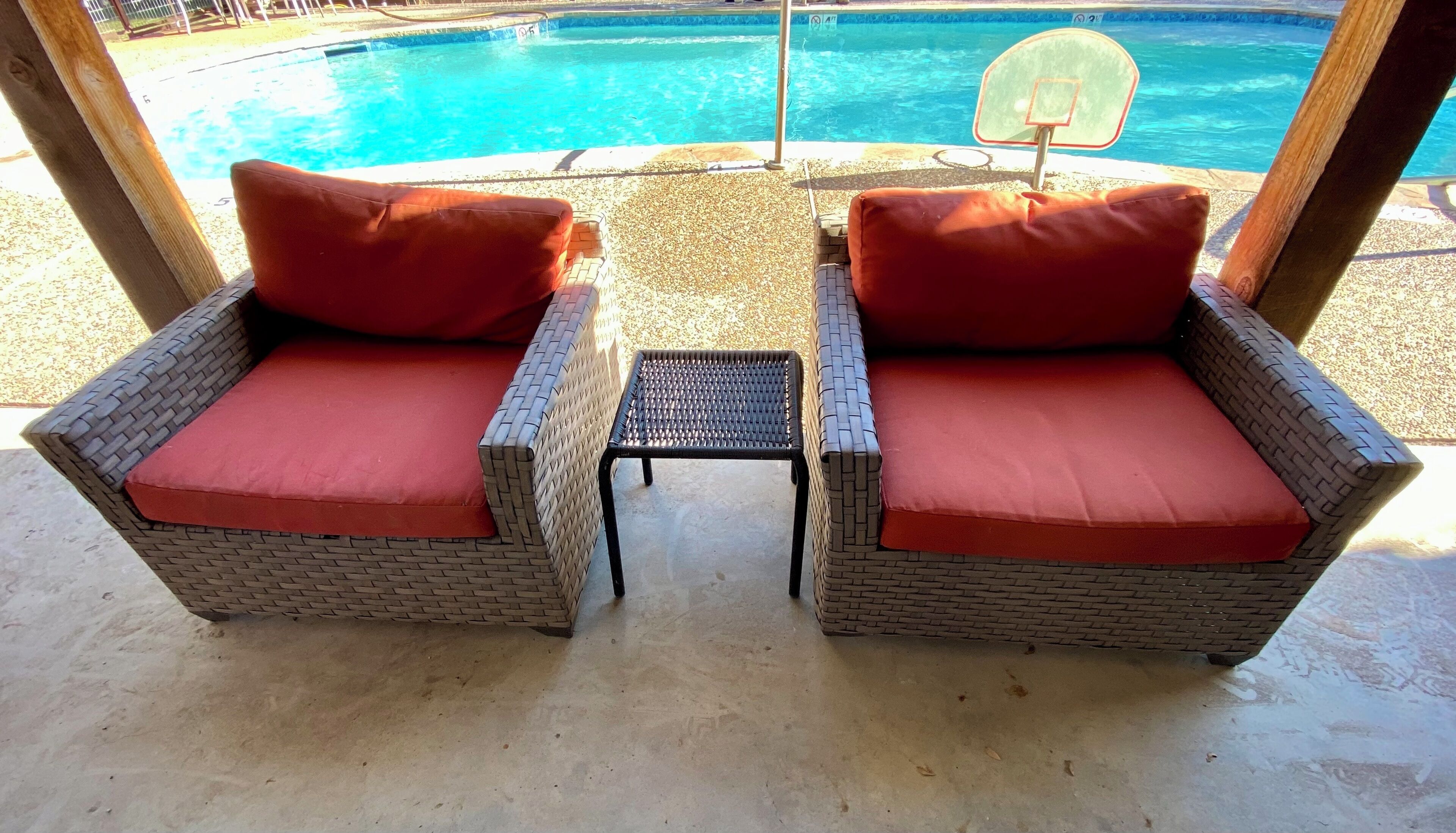 A covered outdoor seating area with wicker chairs and a small table, overlooking a swimming pool.