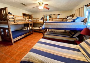 Een studentenkamer met stapelbedden, een plafondventilator en een raam met gordijnen.