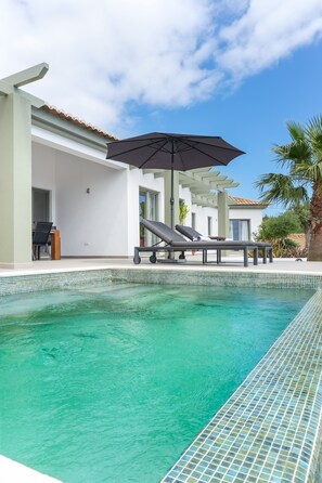 A swimming pool with a tiled edge, a lounge chair, and an umbrella.