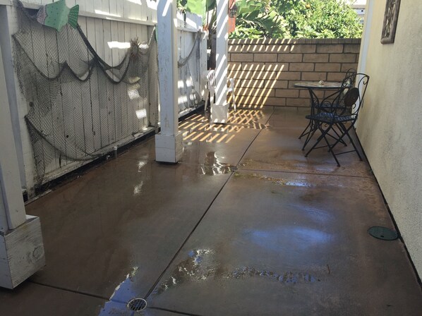 A wet concrete patio with a white fence, a metal gate, and a table with chairs.