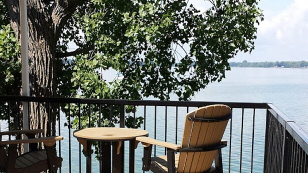 Een houten terras met een tafel en twee Adirondack-stoelen, uitkijkend op het water.