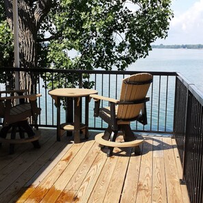 Una terraza de madera con una mesa y dos sillas Adirondack orientadas hacia el agua.