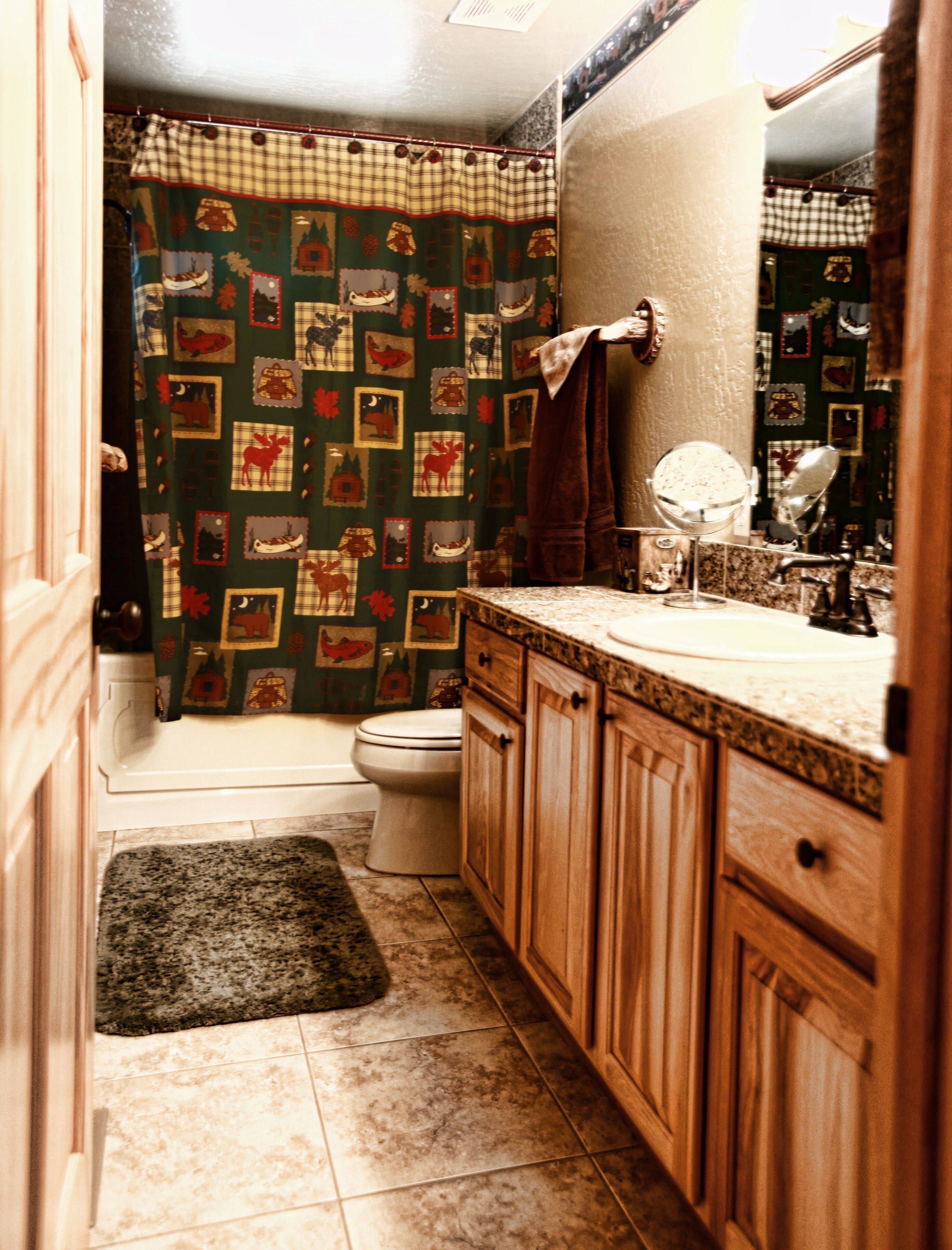 A bathroom with a toilet, sink, and mirror. There is a patterned shower curtain and a rug on the floor.