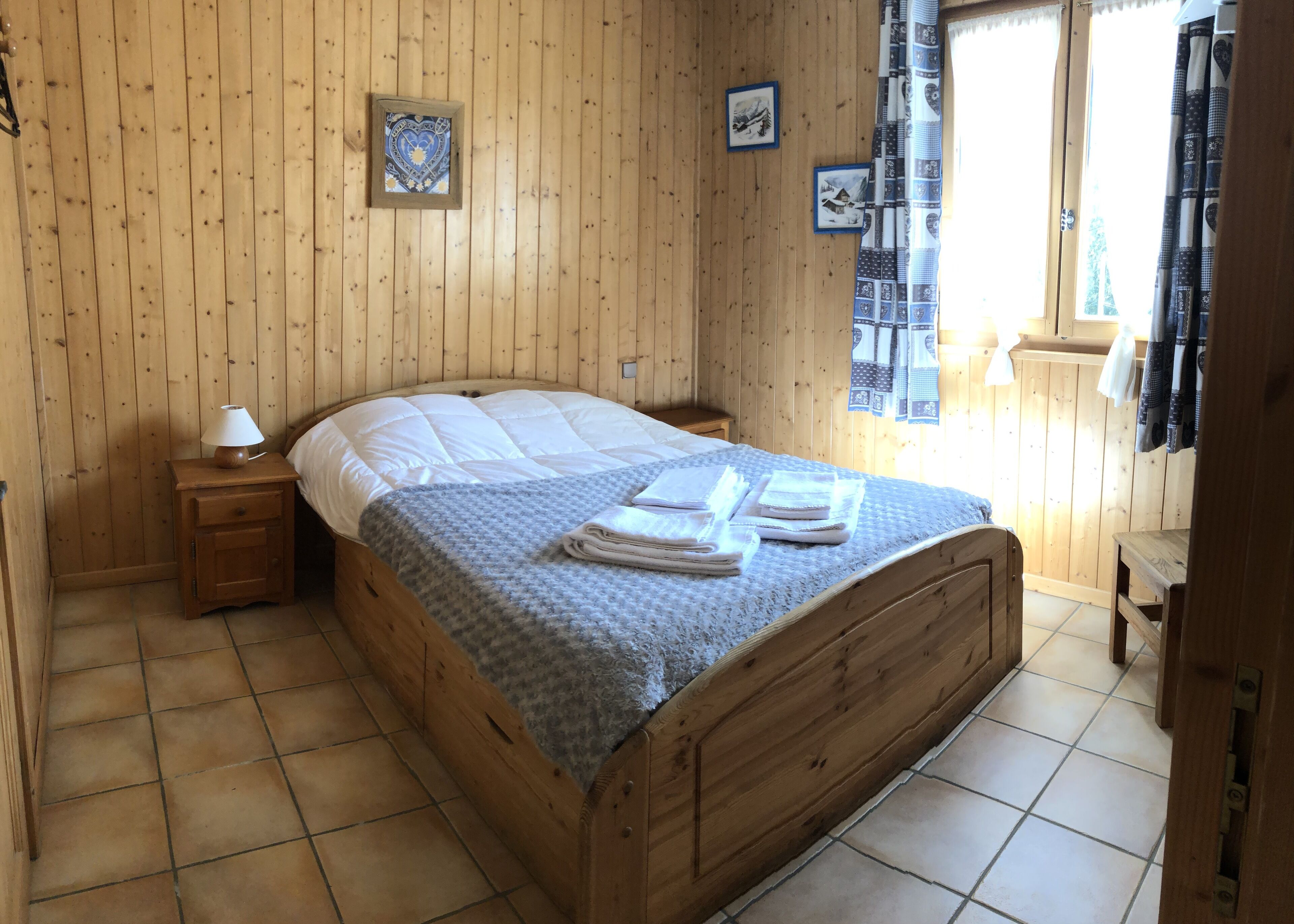 A wooden-paneled room with a bed, a nightstand, and a window with curtains.