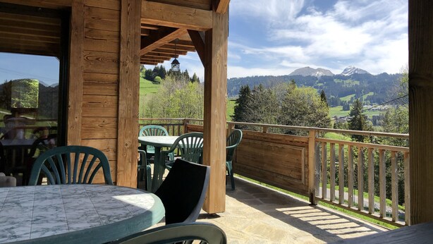 En træterrasse med et bord og stole, med udsigt over et bjerglandskab.