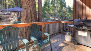 Een terras met Adirondack-stoelen, een barbecue en uitzicht op een bebost gebied.