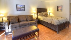 Een slaapkamer met een bed, een bank, een poef, twee lampen en twee ingelijste foto's aan de muur.