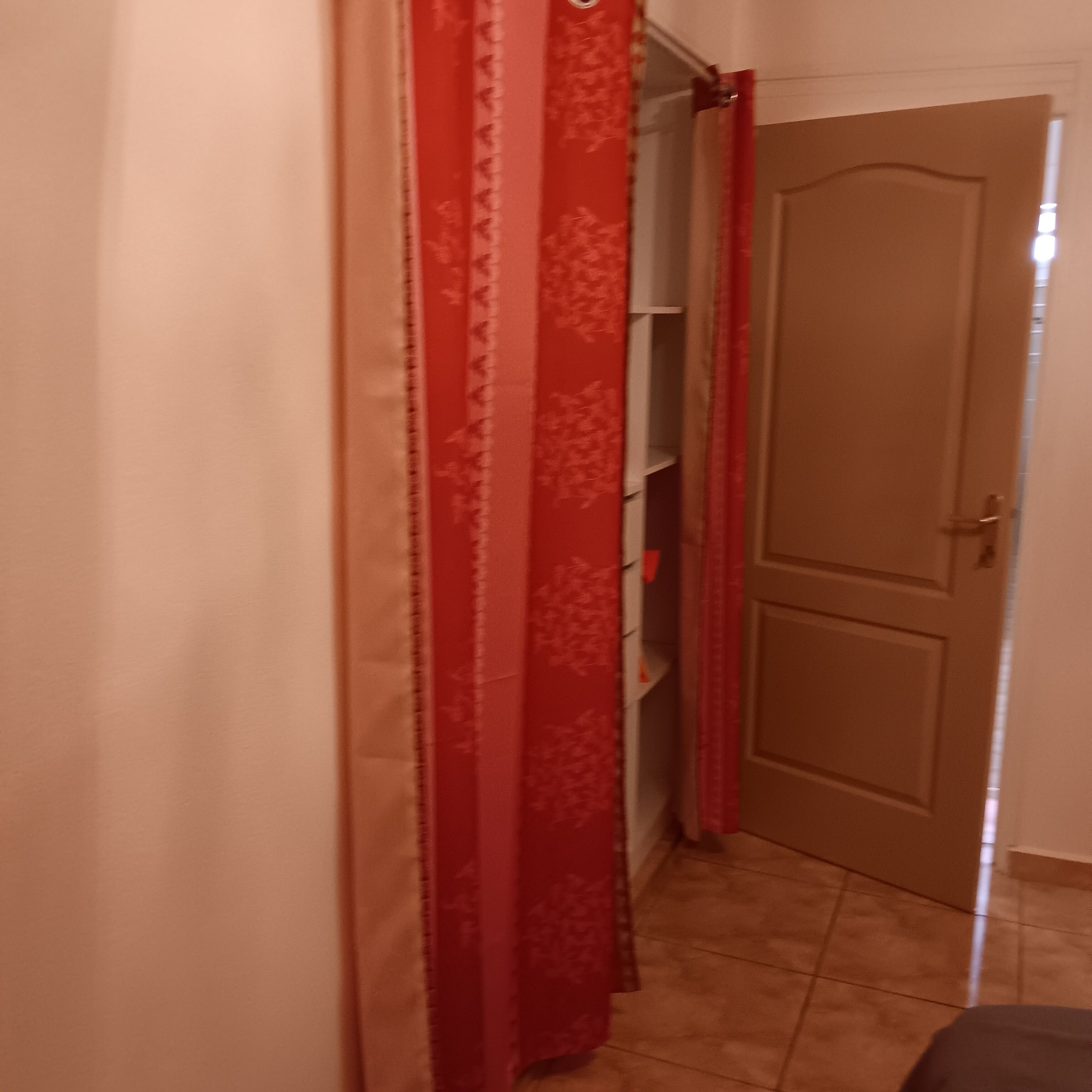 Un pasillo estrecho con una puerta cerrada, una cortina roja y un piso de baldosas.
