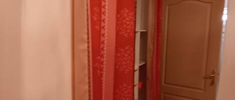 Un pasillo estrecho con una puerta cerrada, una cortina roja y un piso de baldosas.