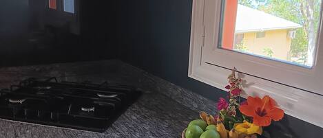 A kitchen with a gas stove, a window with blinds, and a fruit basket on the counter.