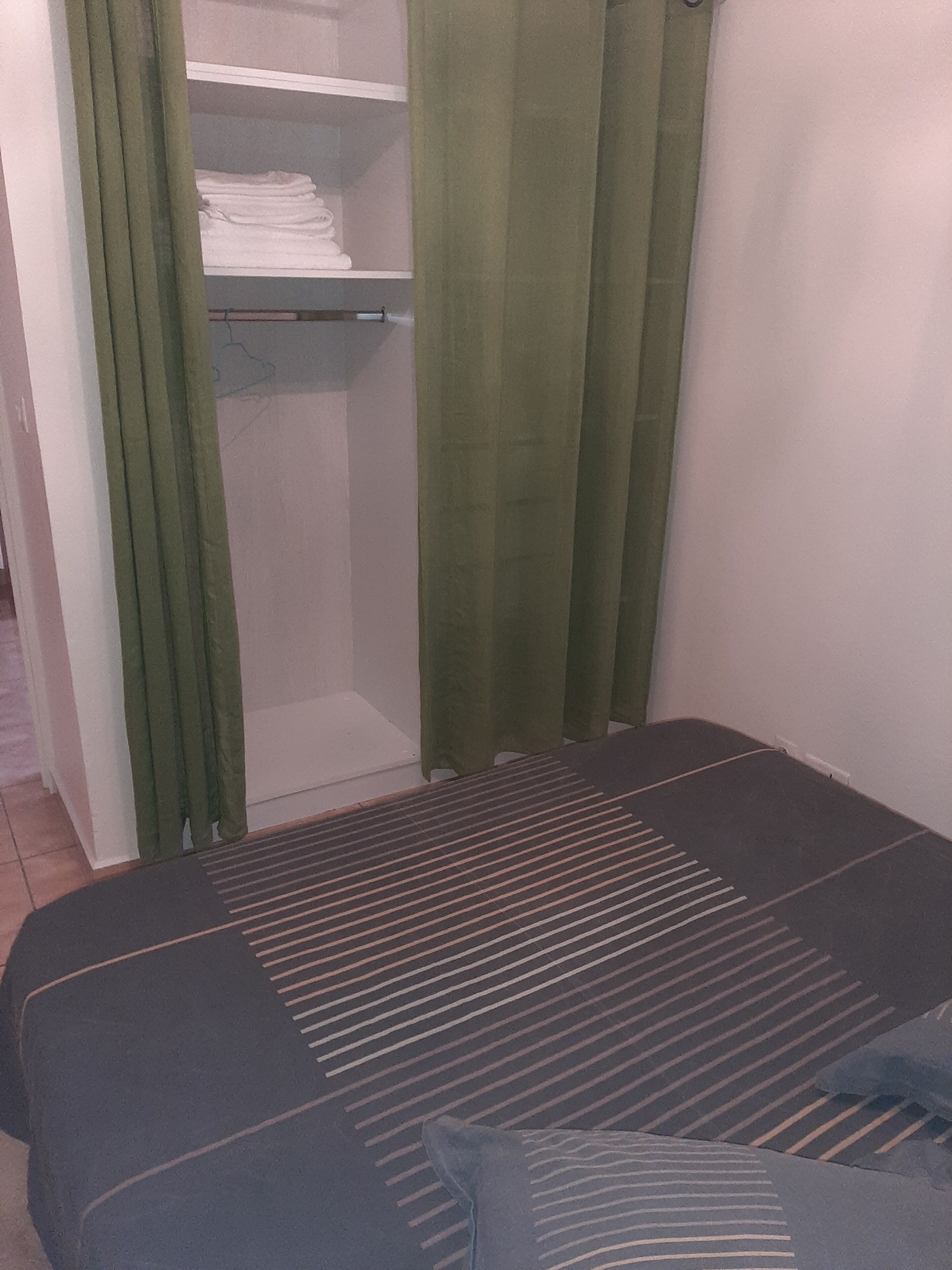 Un dormitorio con una cama, una cortina verde y un armario con toallas dobladas.