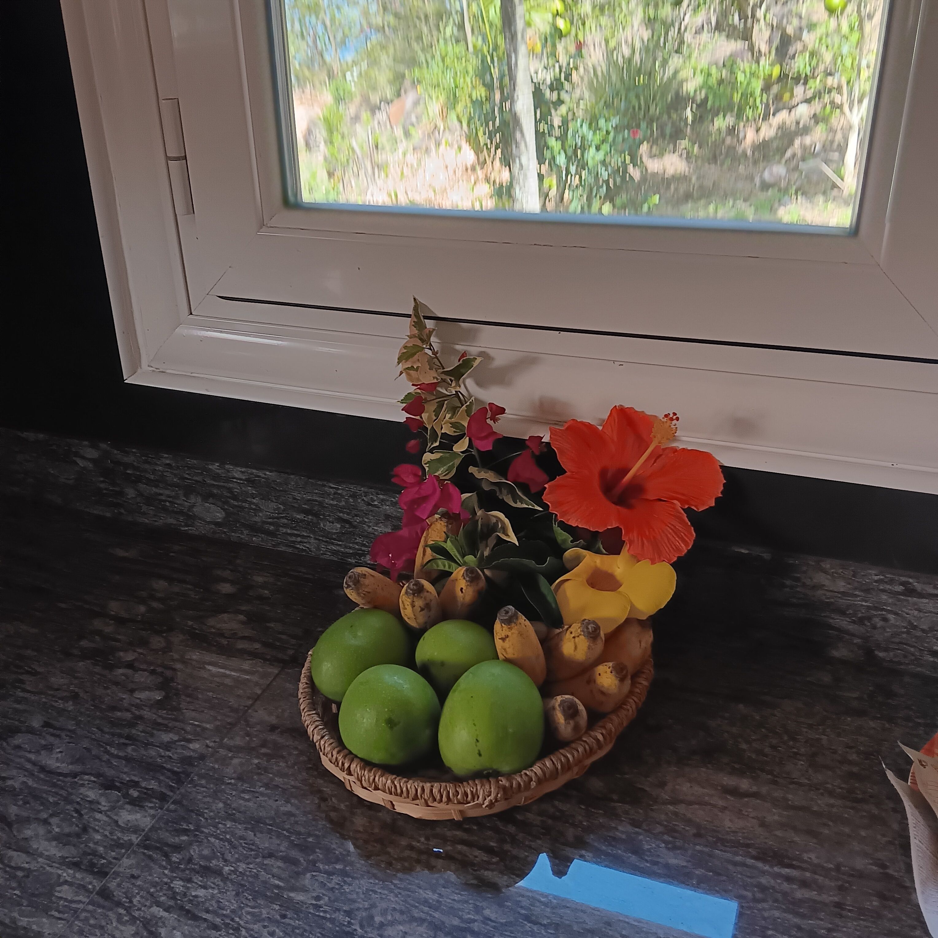 A woven basket with fruits and flowers on a kitchen counter.