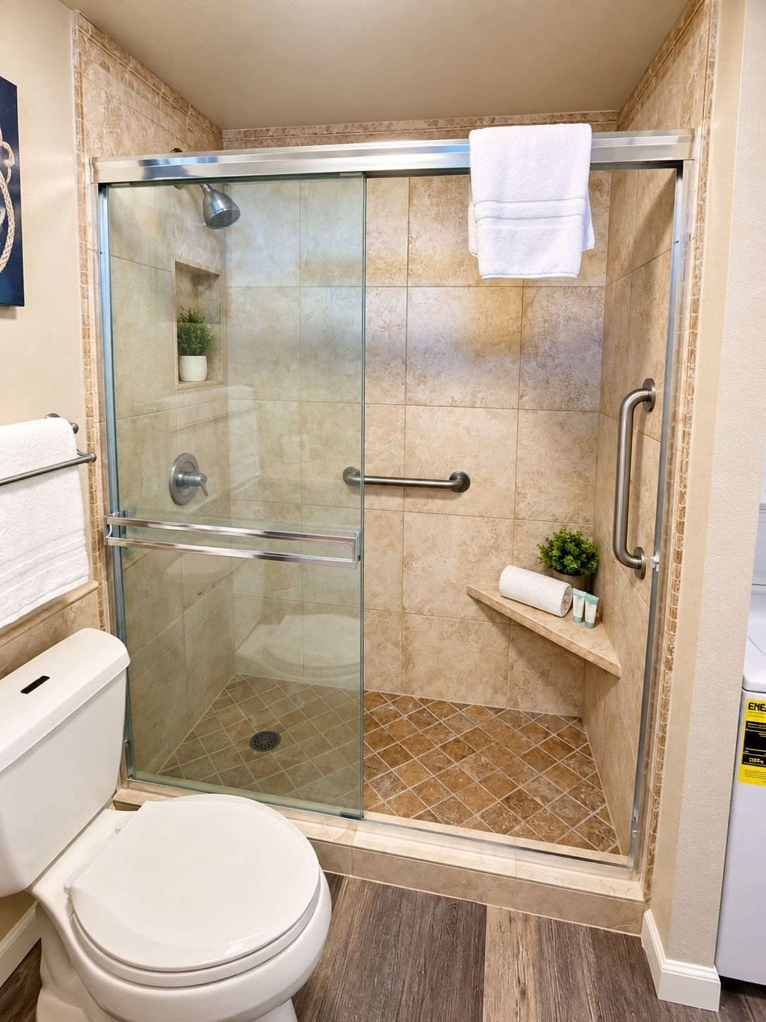 Une cabine de douche fermée par des parois en verre, avec une serviette blanche accrochée à la porte, une petite étagère contenant des articles de toilette et des toilettes avec un abattant blanc.