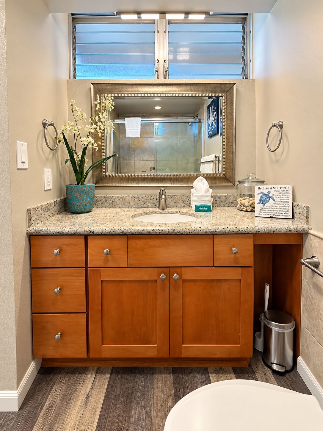 A bathroom with a granite countertop, a wooden vanity, a glass shower enclosure, and a potted orchid.