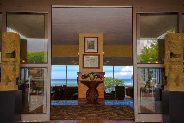A lobby with a large window offering a view of the ocean, a reception desk with a vase of flowers, and a seating area with chairs and a sofa. - Royal Kahana 318 Studio Bedroom Condo by RedAwning (Lahaina)
