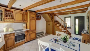 Een keuken met houten kastjes, een fornuis en een eethoek met een tafel voor twee personen.