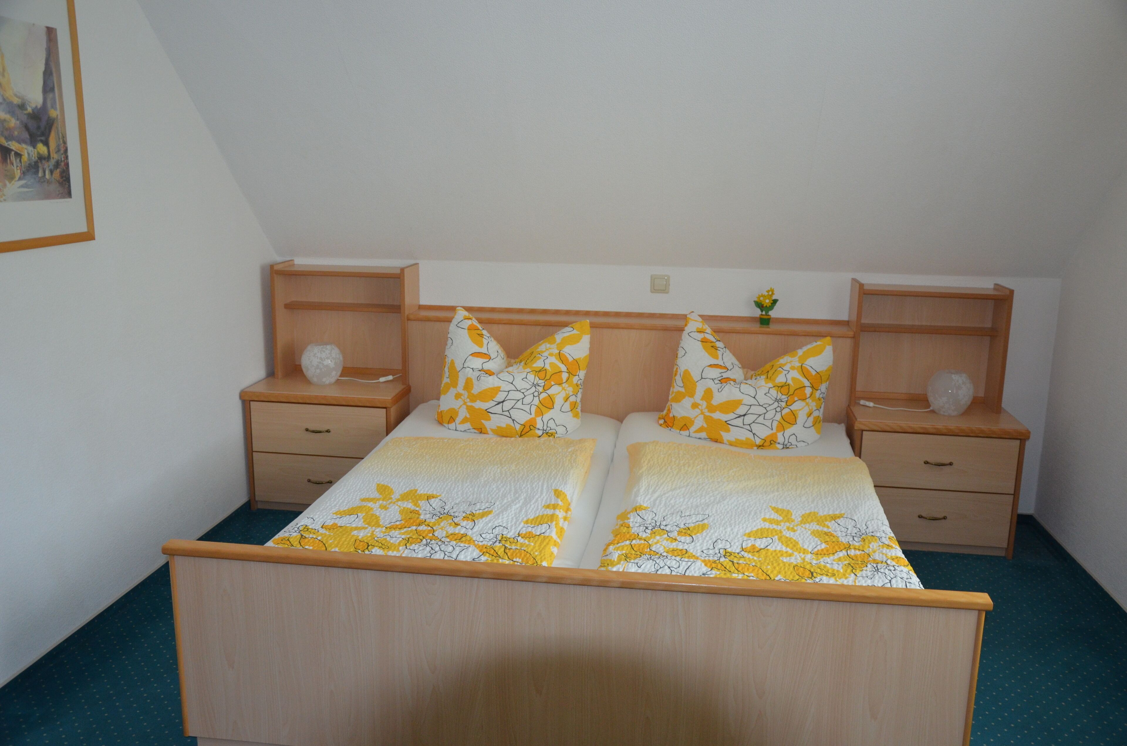 A double bed with a floral bedspread, two nightstands with lamps, and a small vase on the nightstand.
