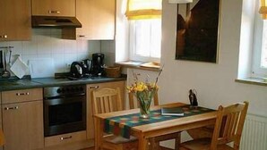 Une petite cuisine avec des meubles en bois, une cuisinière et une table à manger avec des chaises. Un vase rempli de fleurs est posé sur la table.