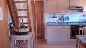 Une cuisine avec des meubles de rangement en bois, un évier en acier inoxydable et une table en bois recouverte d’une nappe à carreaux.