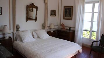 Une chambre à coucher bien rangée, avec un grand lit, une table de chevet avec une lampe, une commode et une chaise.