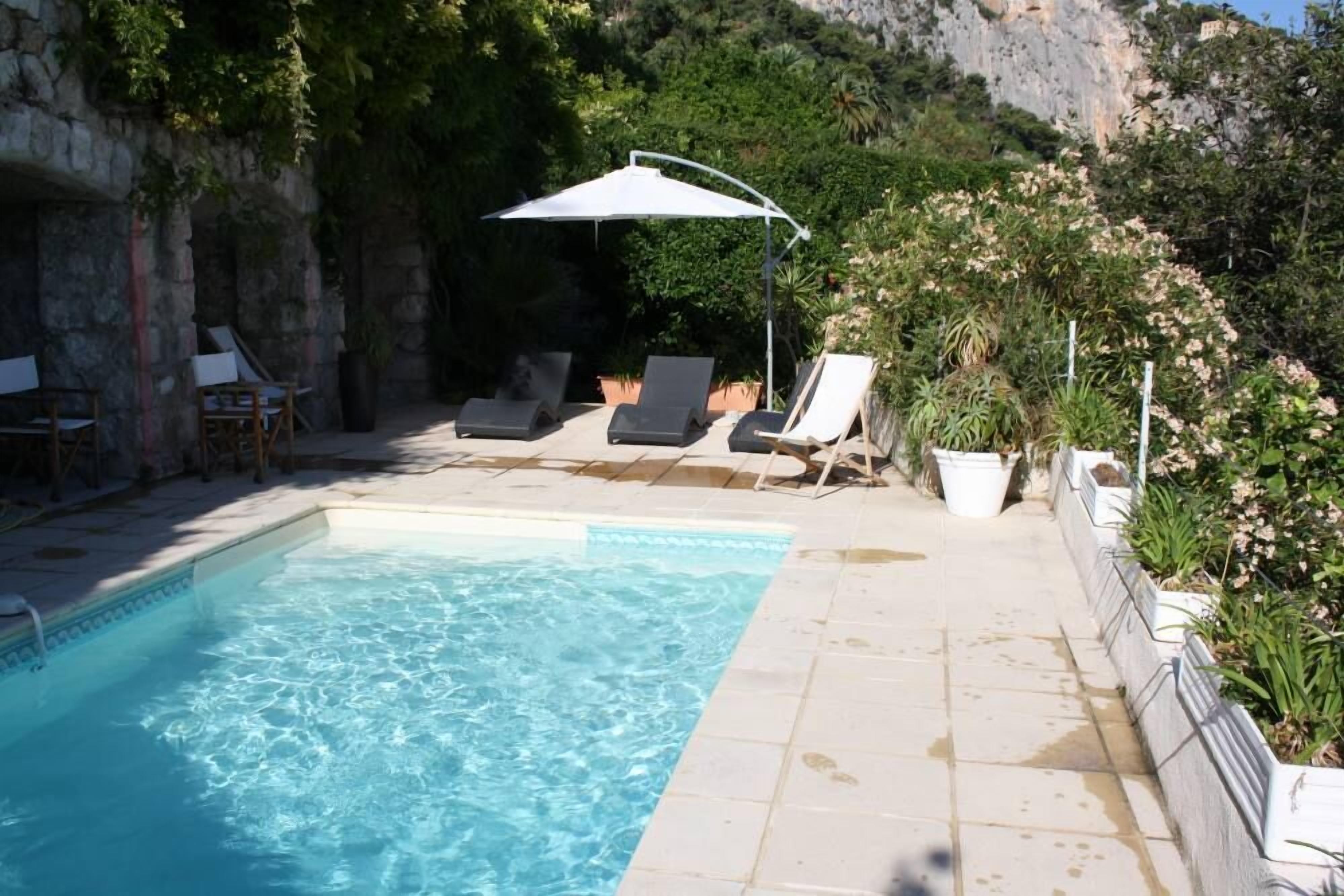 A swimming pool with lounge chairs and umbrellas, surrounded by greenery and stone walls.