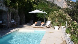 A swimming pool with lounge chairs and umbrellas, surrounded by greenery and stone walls. - House / Villa - Menton (Menton)
