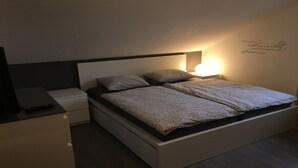 Un dormitorio moderno con cama, mesitas de noche y una lámpara fijada a la pared.
